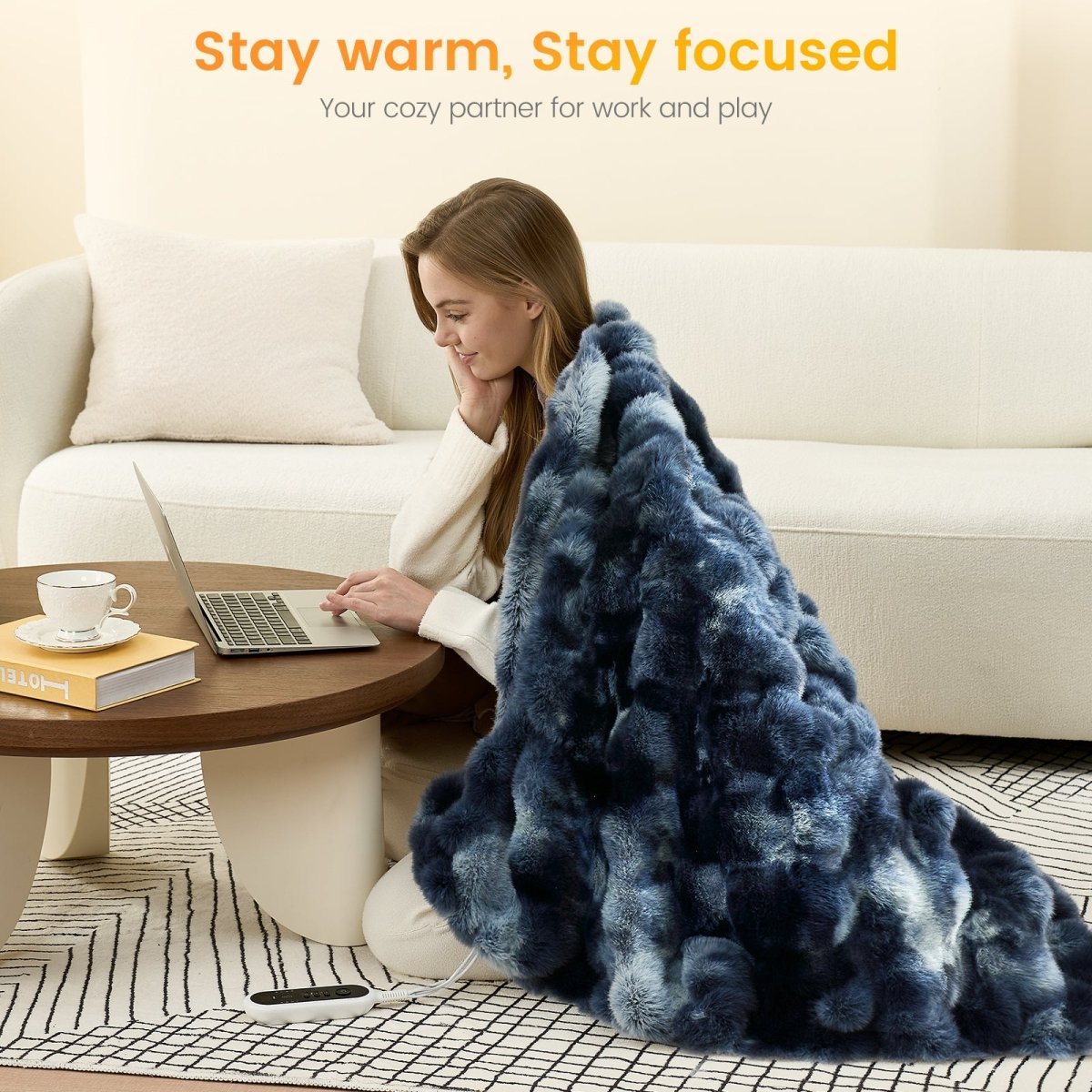 Woman using a laptop on a coffee table with a tie-dye blue faux fur heated electric throw blanket draped over her, sitting on the floor in a cozy living room.   #color_Tie-dye Blue